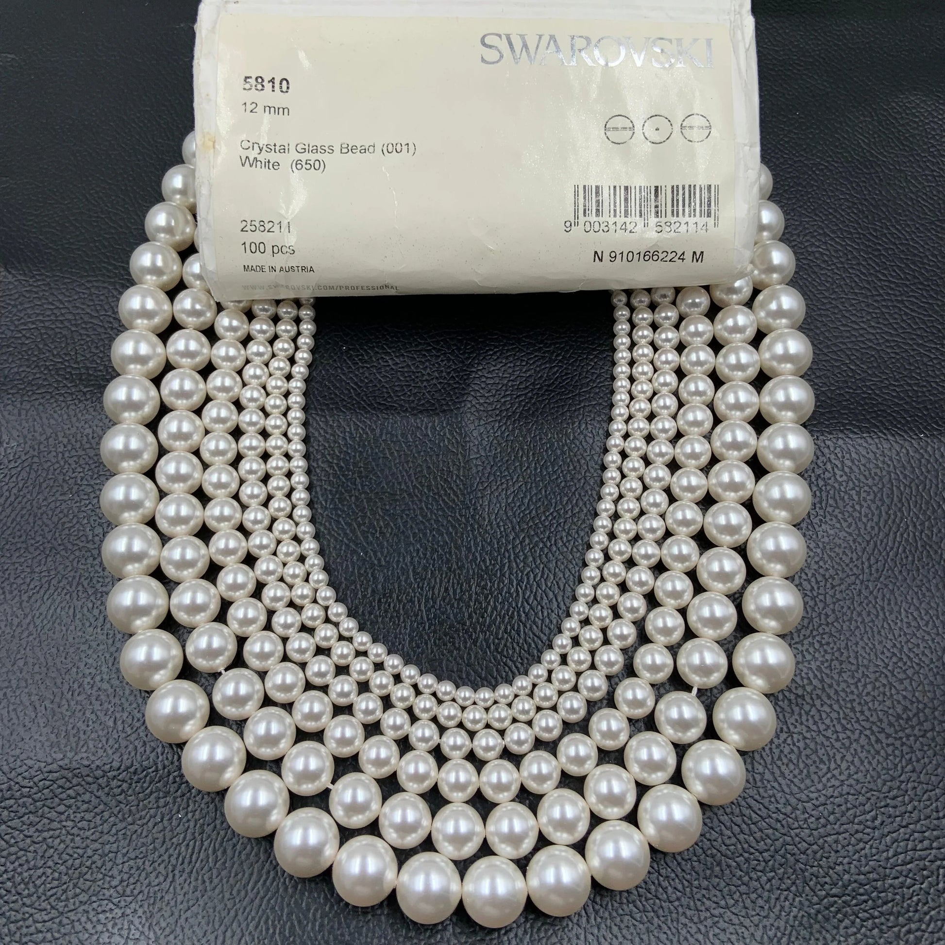 Strands of white Swarovski crystal glass pearl beads in graduated sizes on black background.