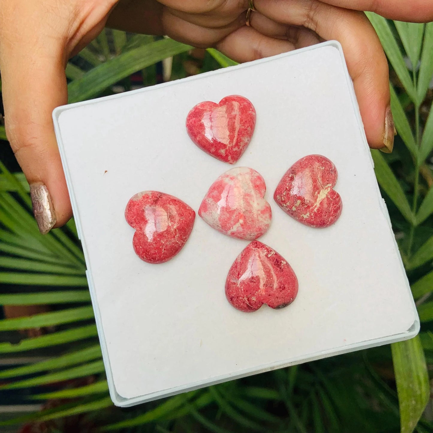 Hand holding box with five polished pink heart-shaped gemstone cabochons on display.