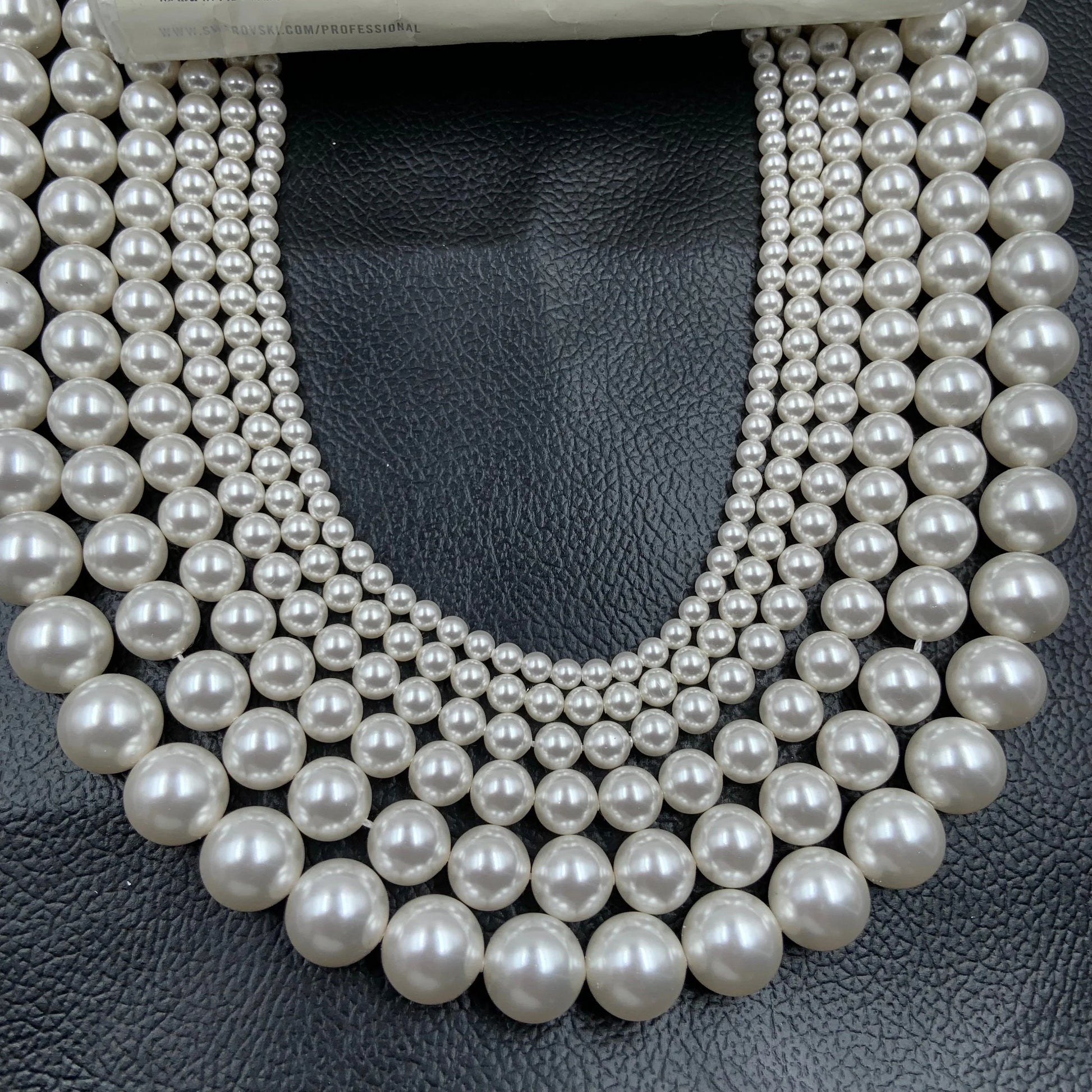 Strands of round white gemstone beads in graduated sizes on black leather background.