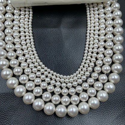 Strands of round white gemstone beads in graduated sizes on black leather background.