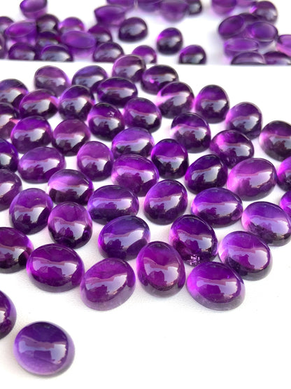 Glossy oval amethyst cabochon gemstones scattered on a white surface