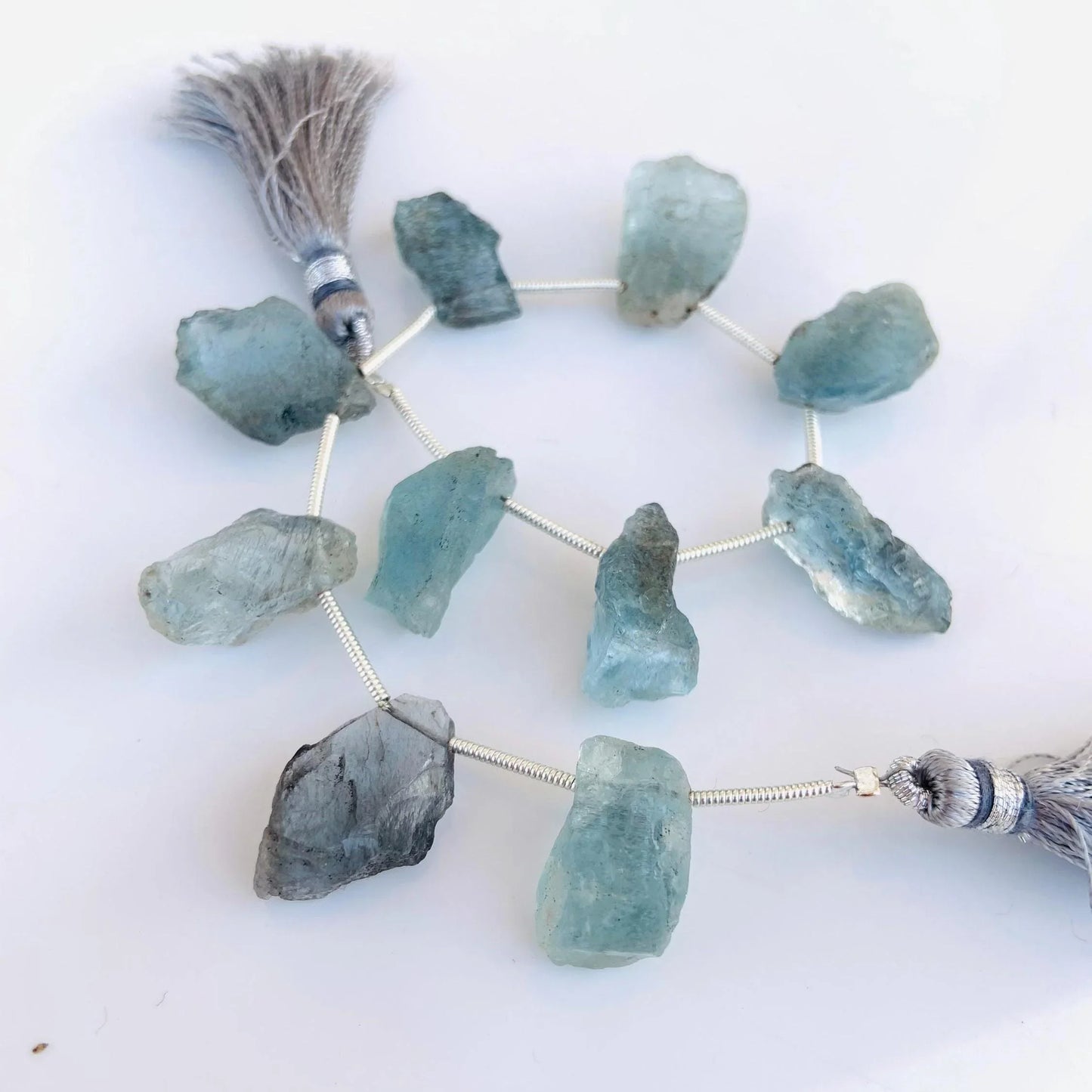 Natural rough aquamarine gemstone beads with gray tassels on a white background