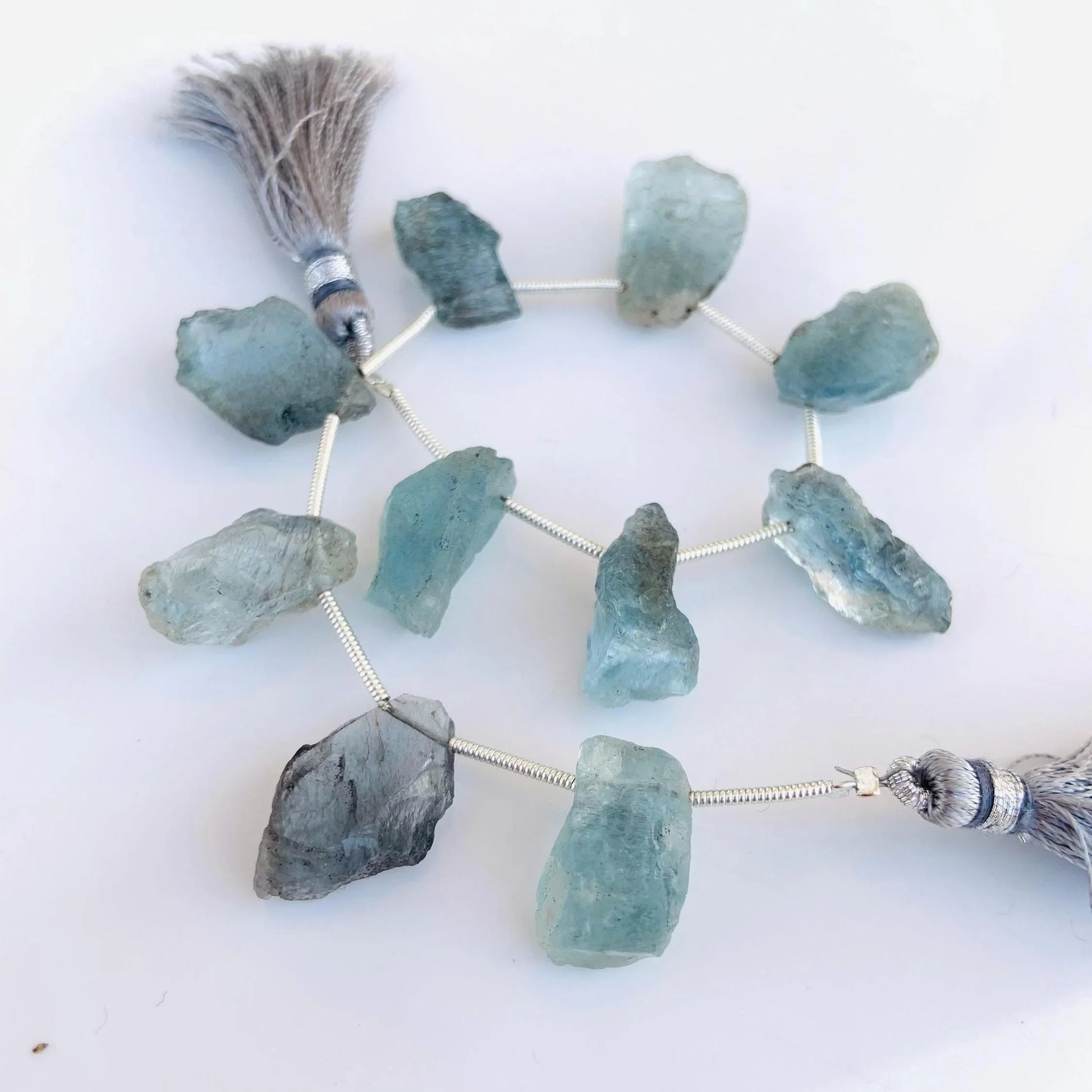 Natural rough aquamarine gemstone beads with gray tassels on a white background