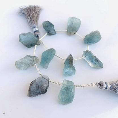 Natural rough aquamarine gemstone beads with gray tassels on a white background