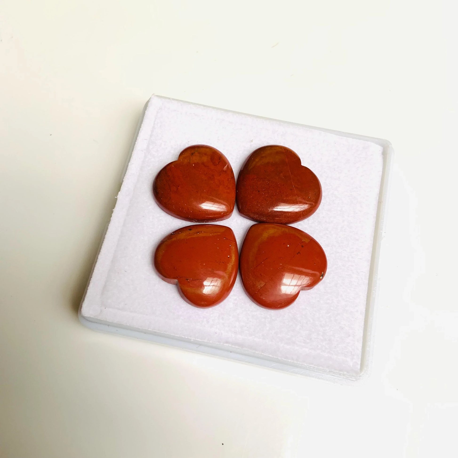 Four heart-shaped red jasper gemstone cabochons on white display pad