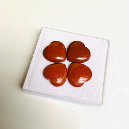 Four heart-shaped red jasper gemstone cabochons on white display pad
