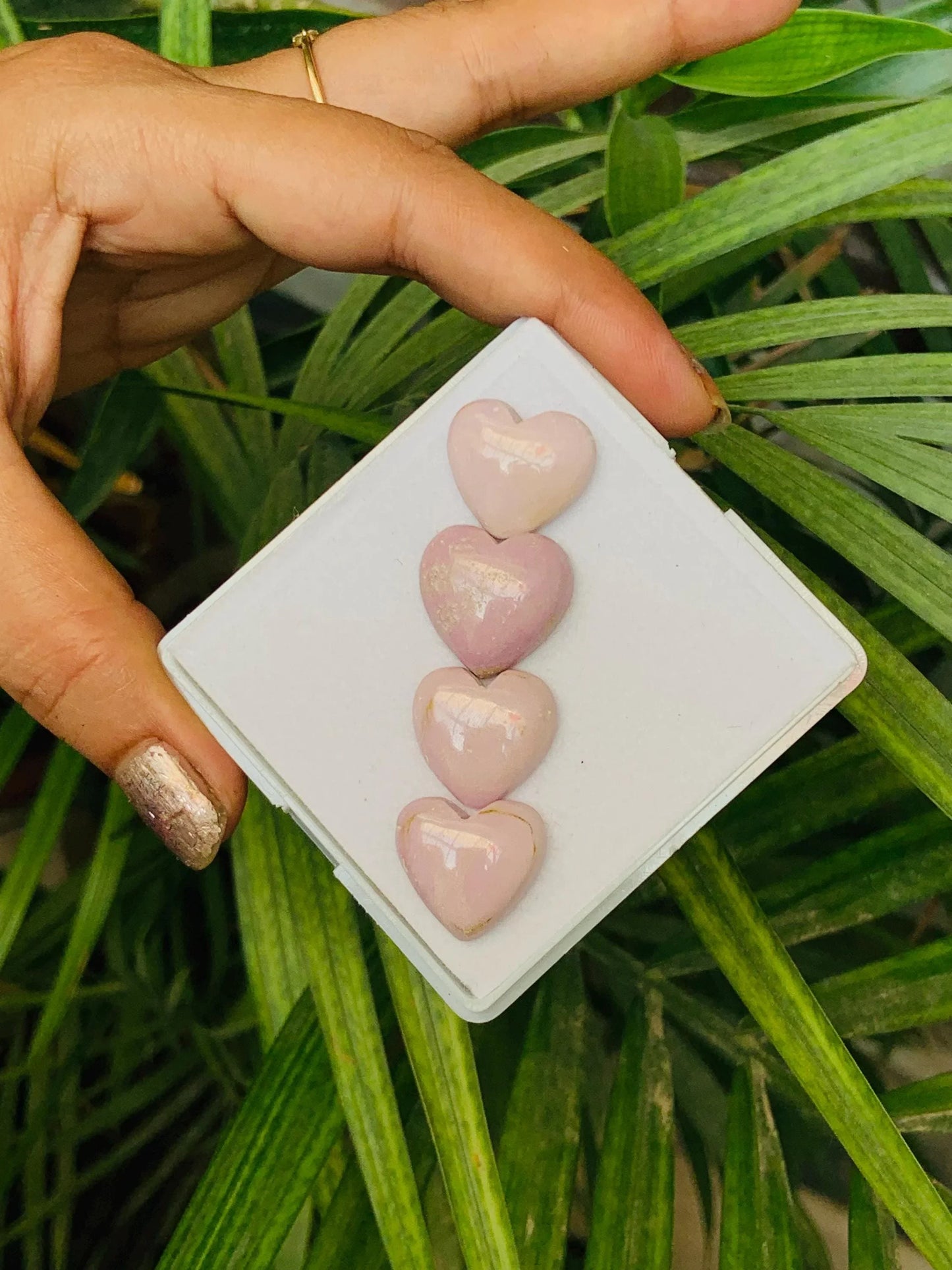 Hand holding a tray with four polished pink heart-shaped gemstone beads.