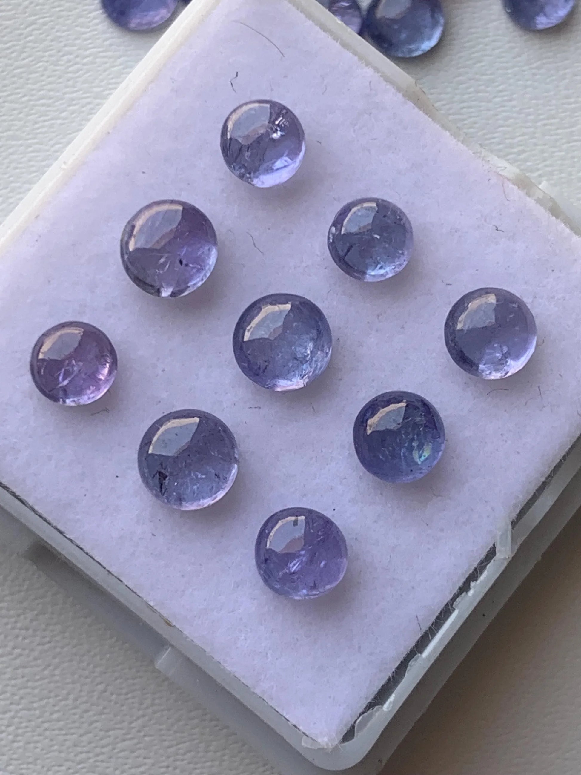 Round natural purple gemstone cabochons displayed on white foam tray