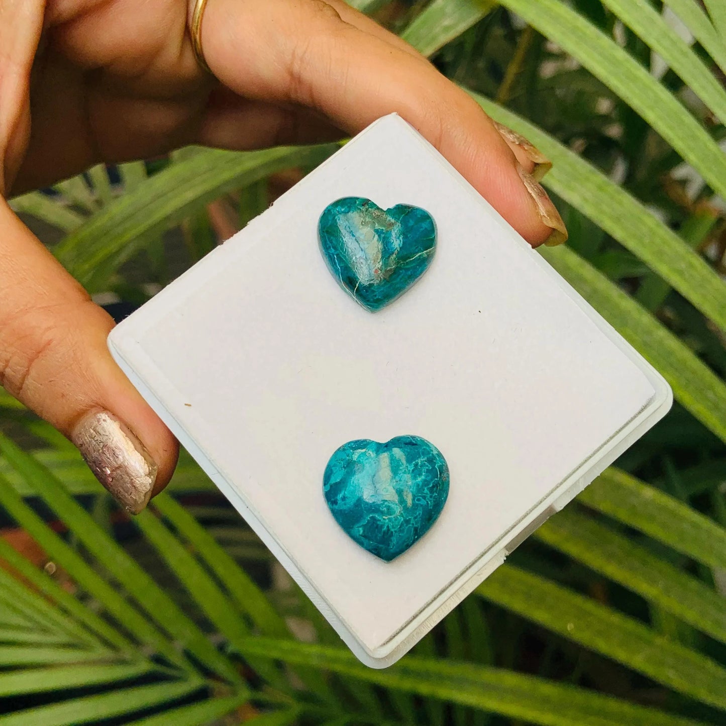 Hand holding two heart-shaped blue gemstone cabochons on a white display card