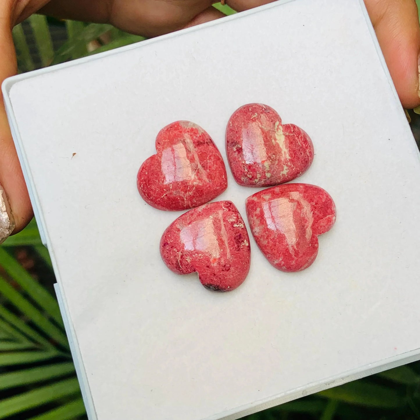 Four heart-shaped pink gemstone cabochons displayed on a white square tray