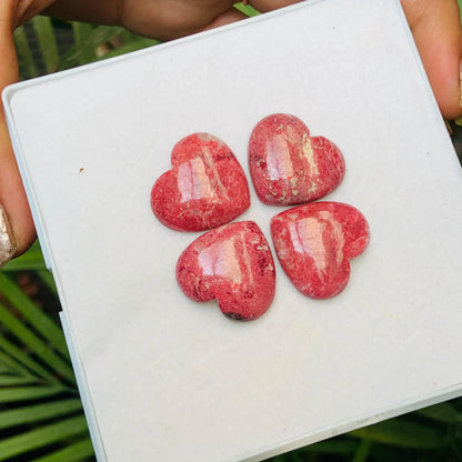 Four heart-shaped pink gemstone cabochons displayed on a white square tray