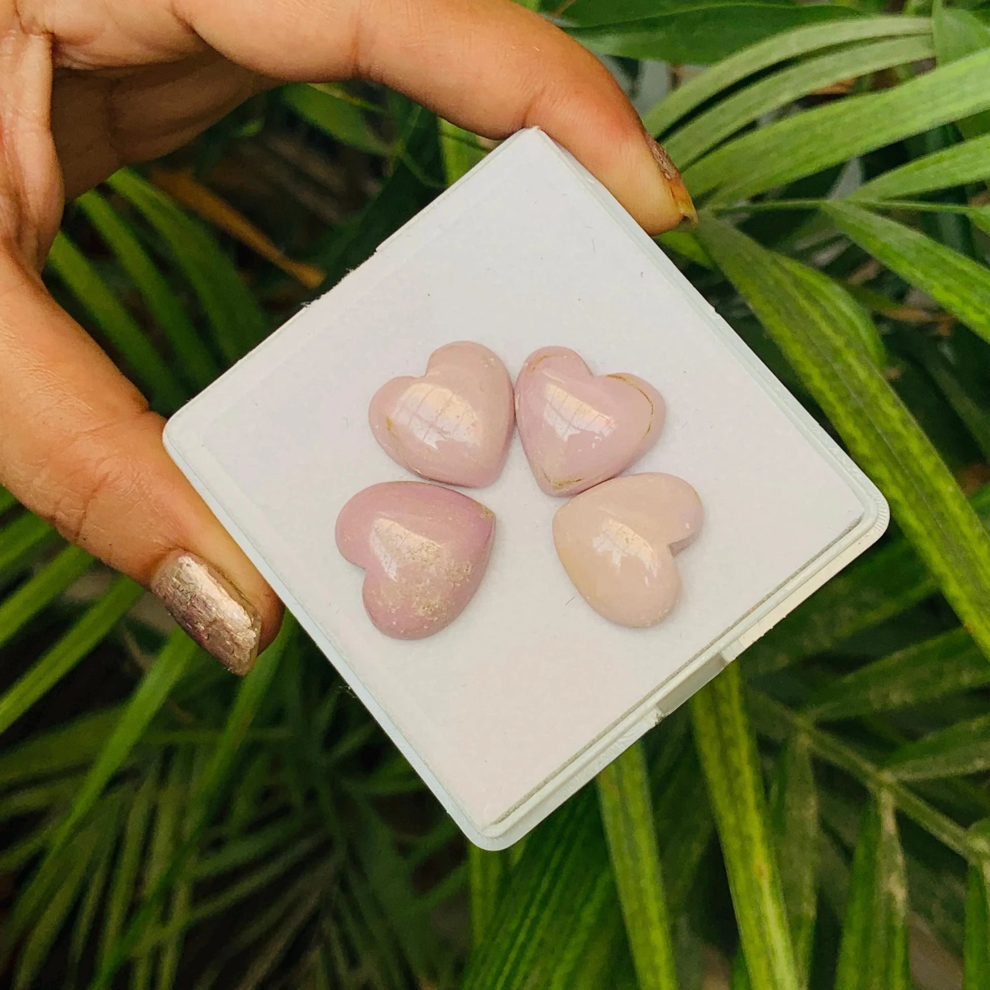 Four pink heart-shaped natural gemstone beads displayed on a white tray, hand holding