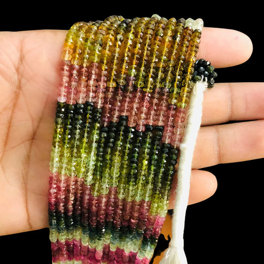 Hand holding multicolored natural tourmaline gemstone bead strands for jewelry making