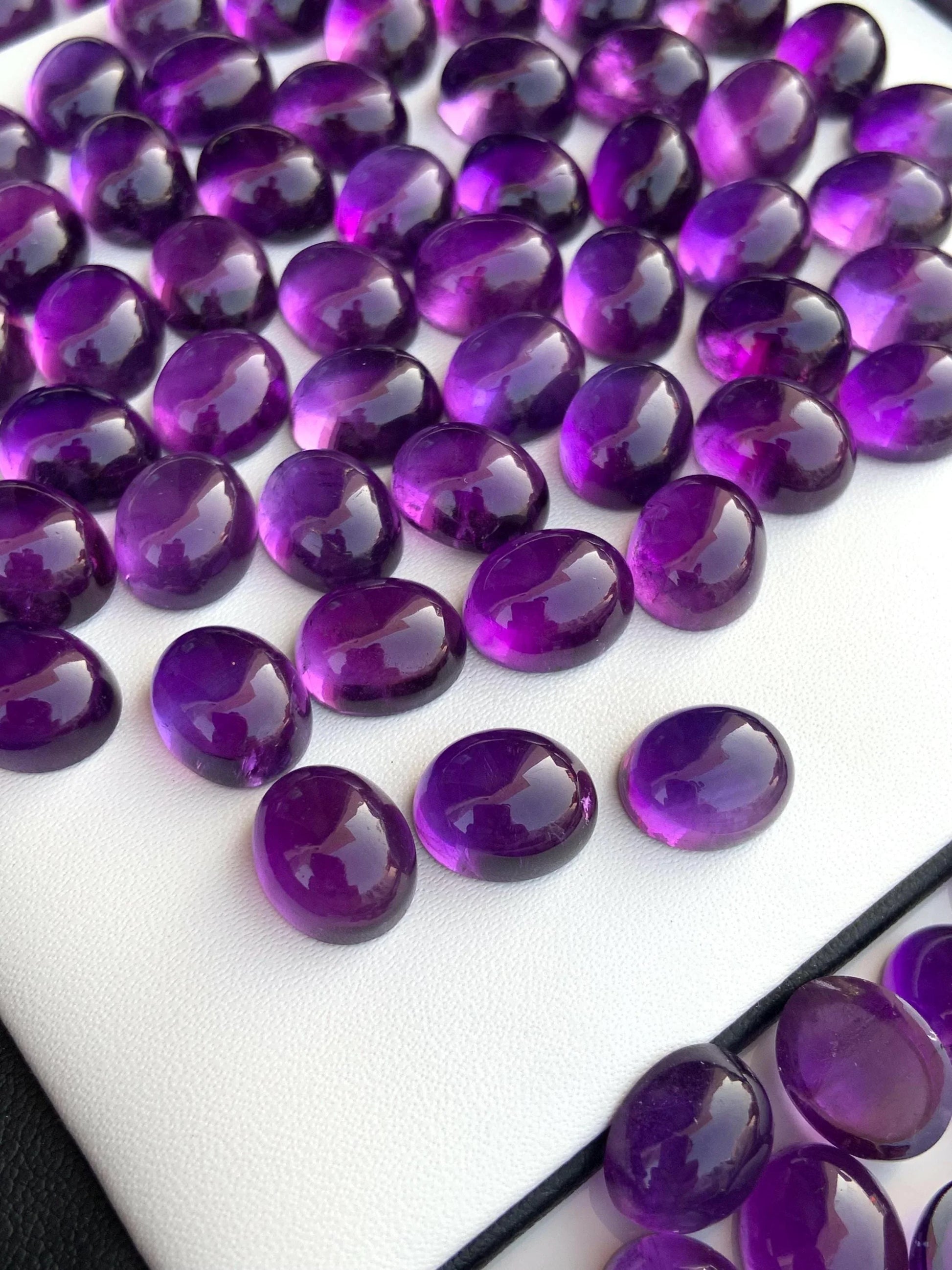 Oval polished amethyst cabochon gemstones on white display background