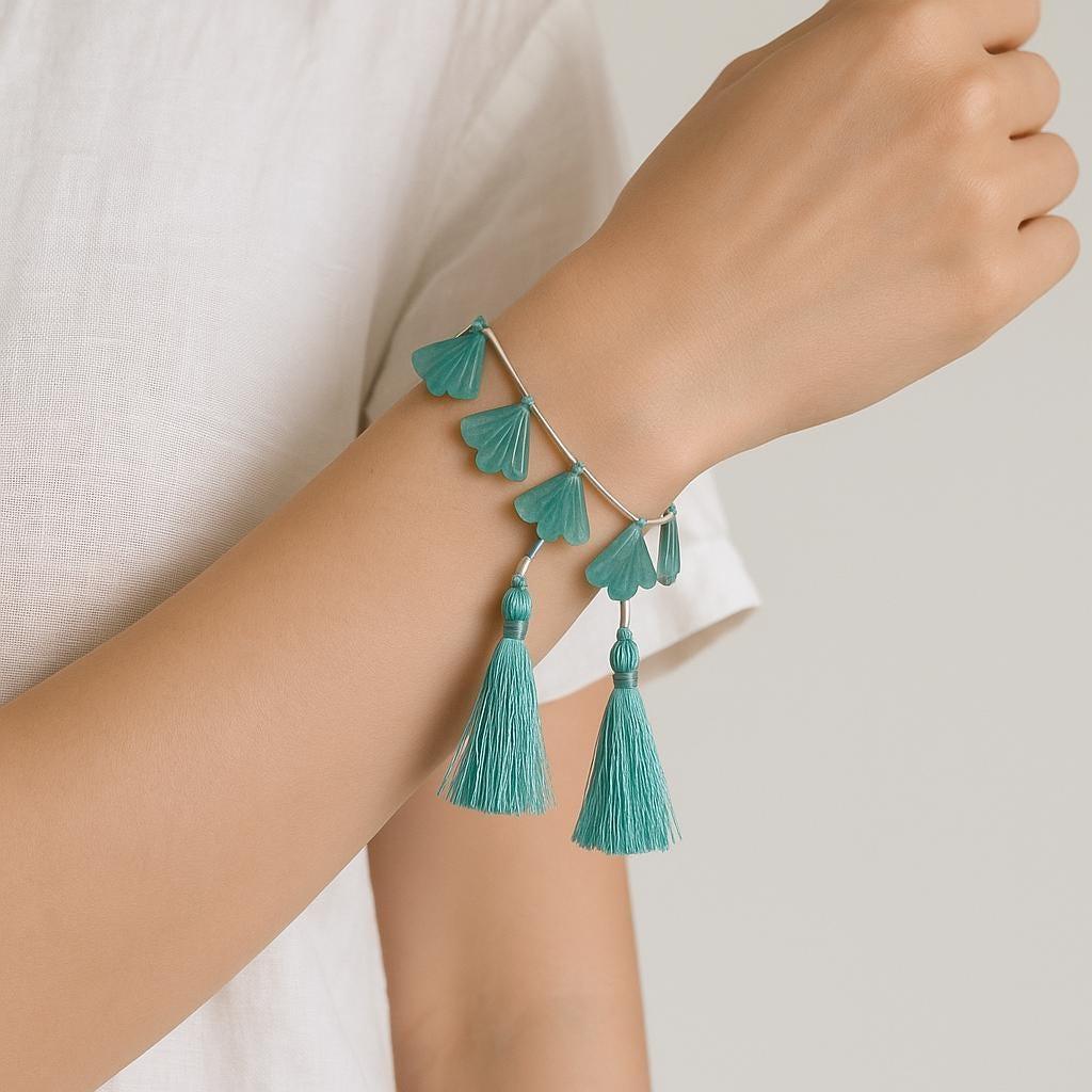 Hand wearing a silver bracelet with teal gemstone petals and tassel charms, minimalist style