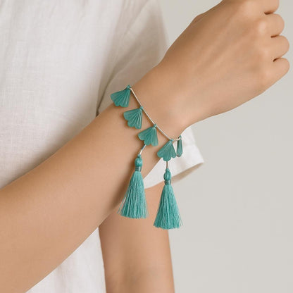 Hand wearing a silver bracelet with teal gemstone petals and tassel charms, minimalist style