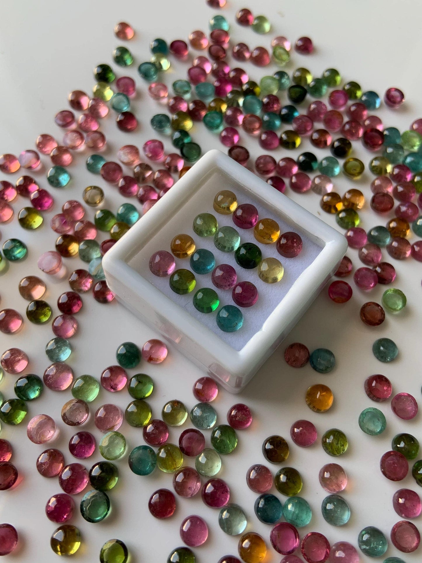 Mixed color round tourmaline cabochon gemstone beads scattered on a white surface