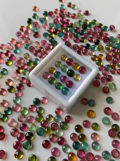 Mixed color round tourmaline cabochon gemstone beads scattered on a white surface