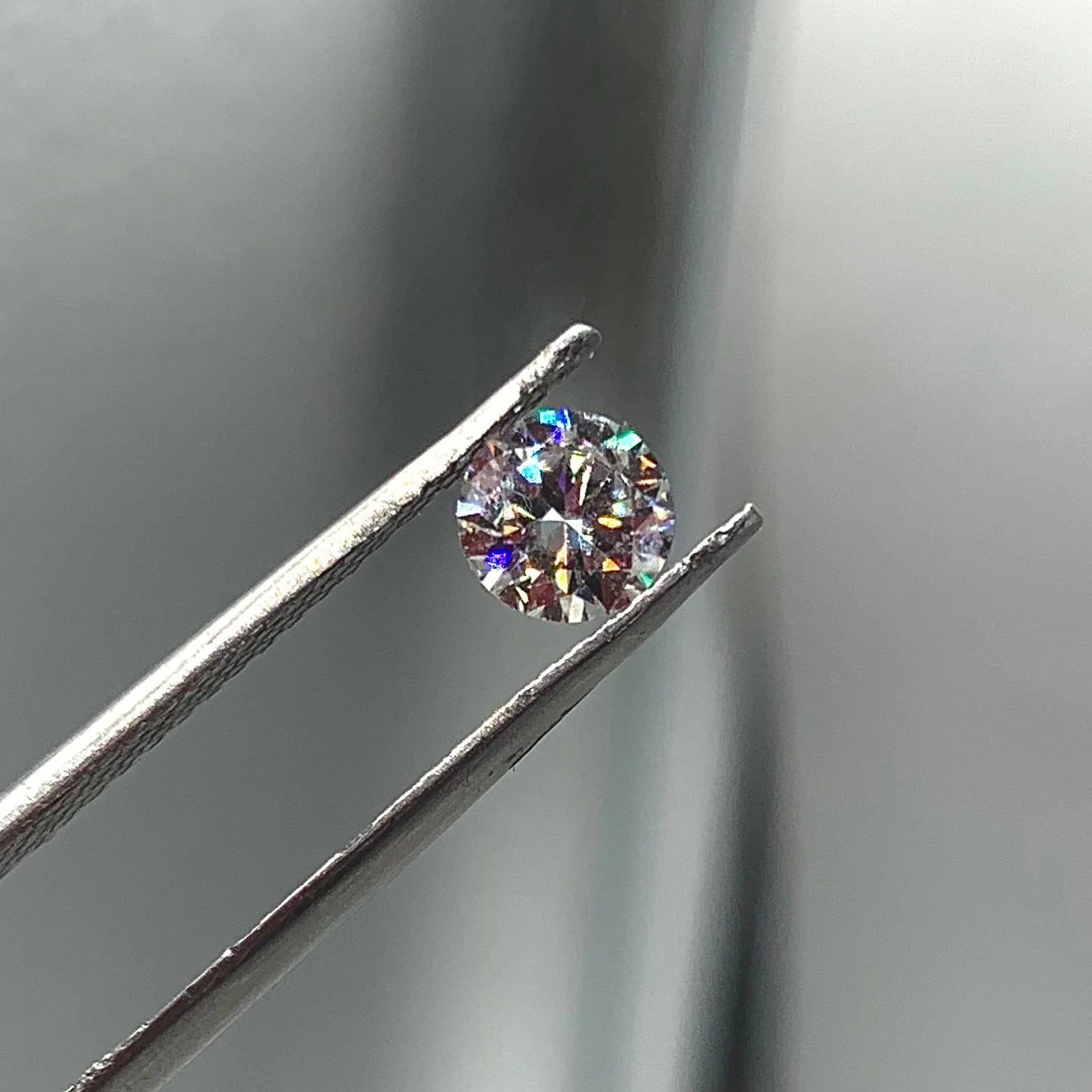 Round brilliant cut gemstone held by tweezers, sparkling facets, close-up