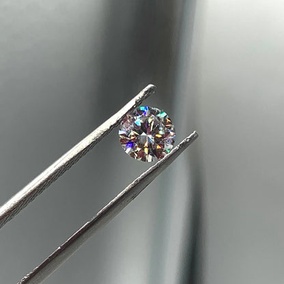 Round brilliant cut gemstone held by tweezers, sparkling facets, close-up