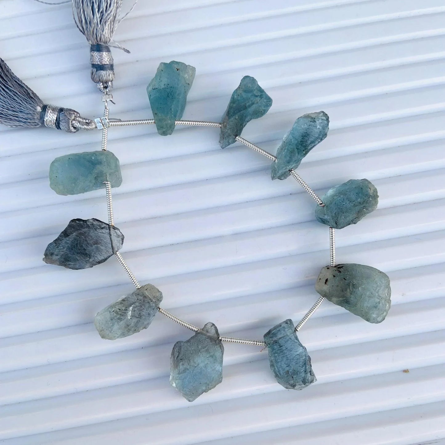 Strand of raw aquamarine gemstone beads with tassels on a white textured background