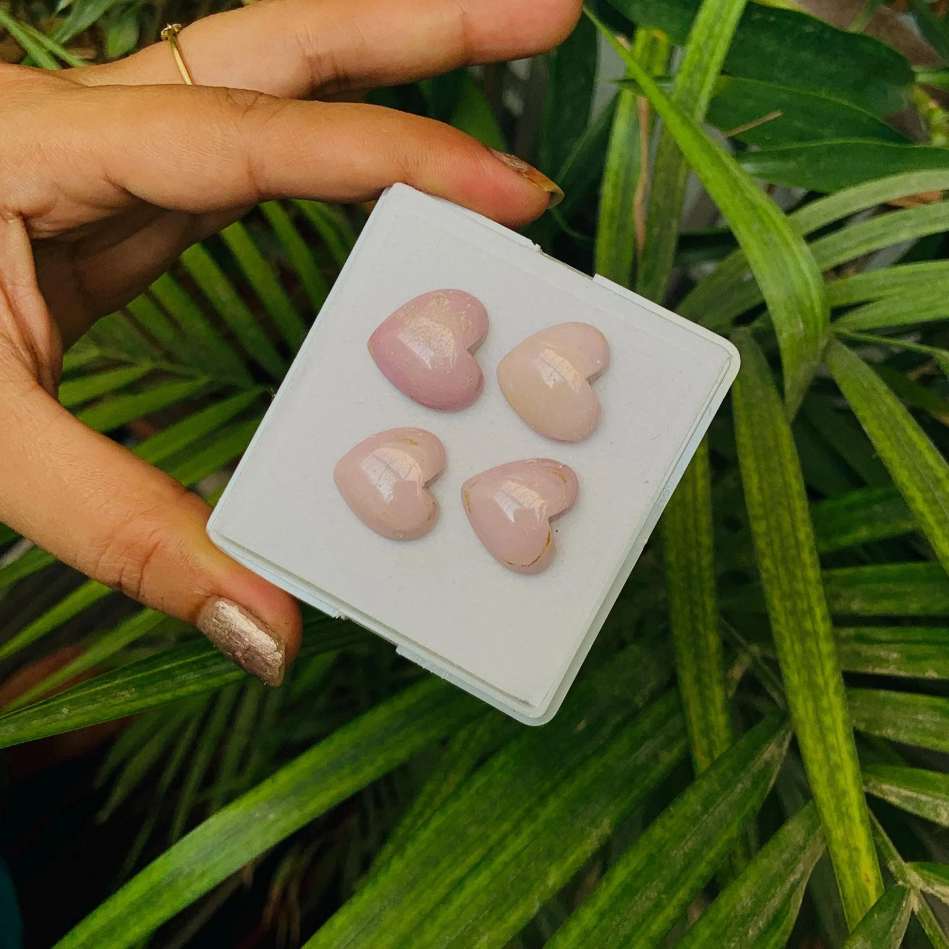 Hand holding box with four polished pink heart-shaped gemstone beads outdoors
