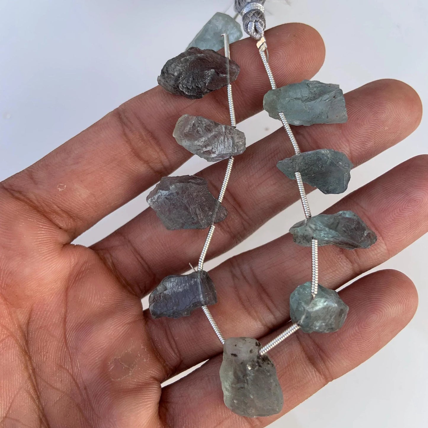Hand holding a strand of raw aquamarine gemstone beads for jewelry making