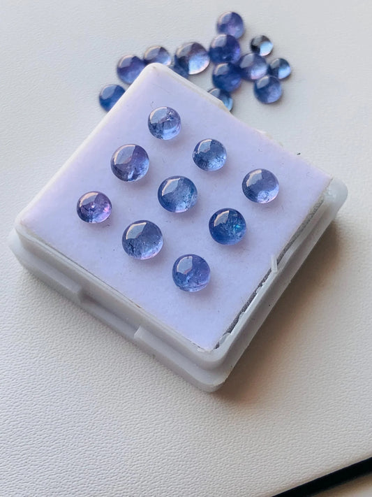 Round blue tanzanite gemstone cabochons displayed on a white case for jewelry making.