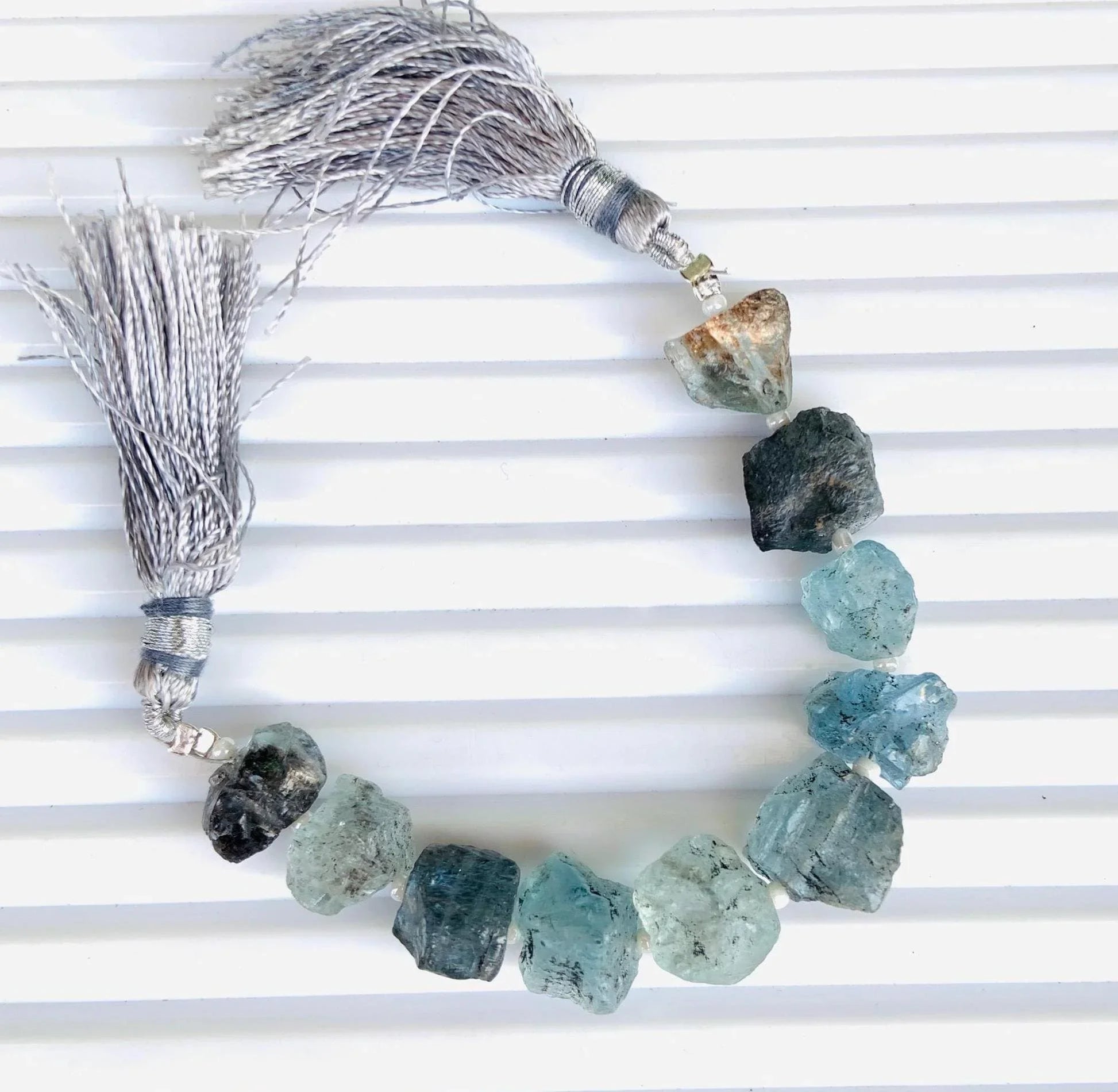 Strand of raw aquamarine gemstone beads with silver tassels on a white background