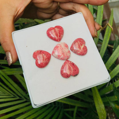 Hand holding a box with five pink heart-shaped natural gemstone cabochons