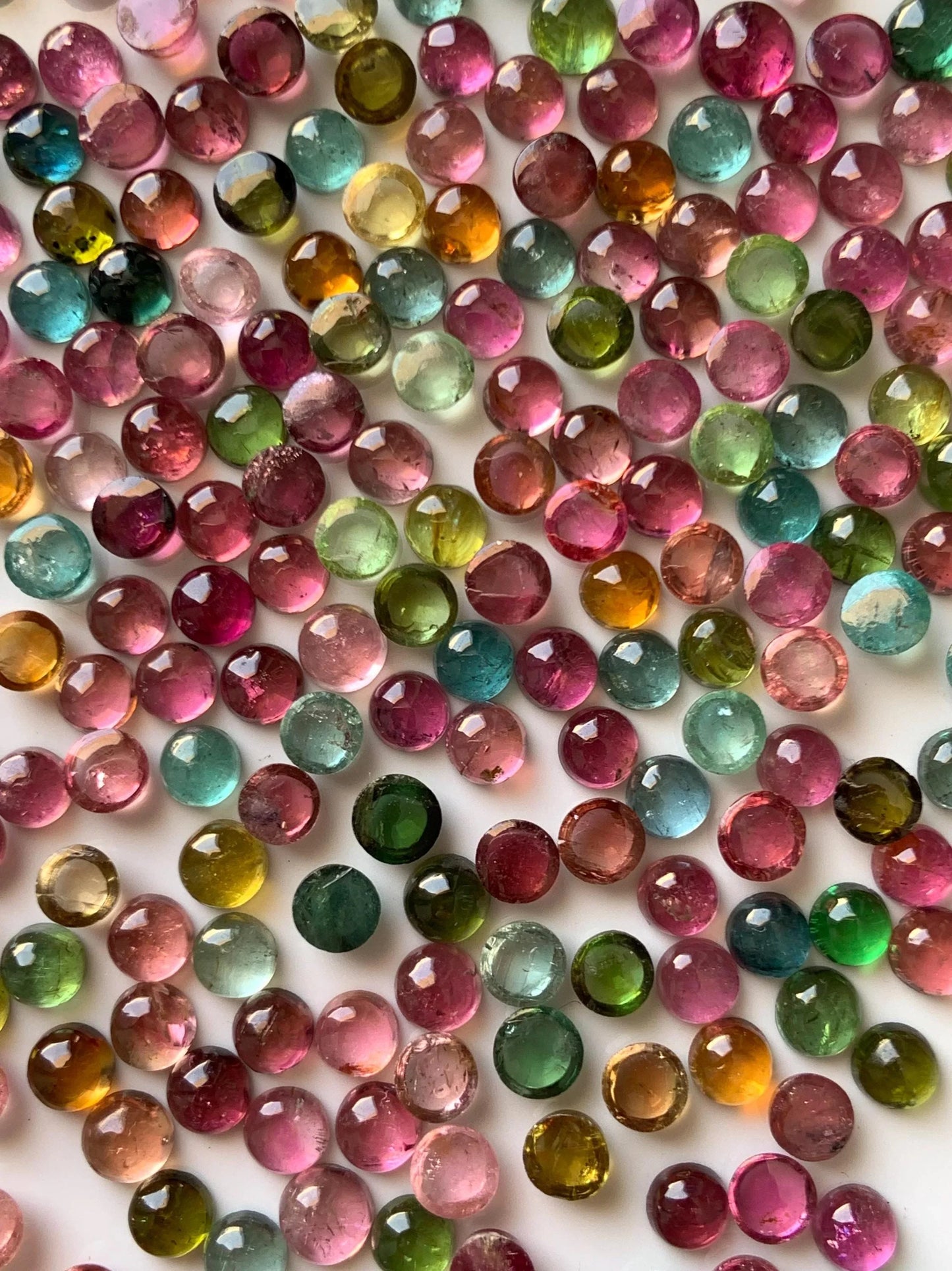 Assorted round multicolor natural tourmaline cabochon gemstones on white background