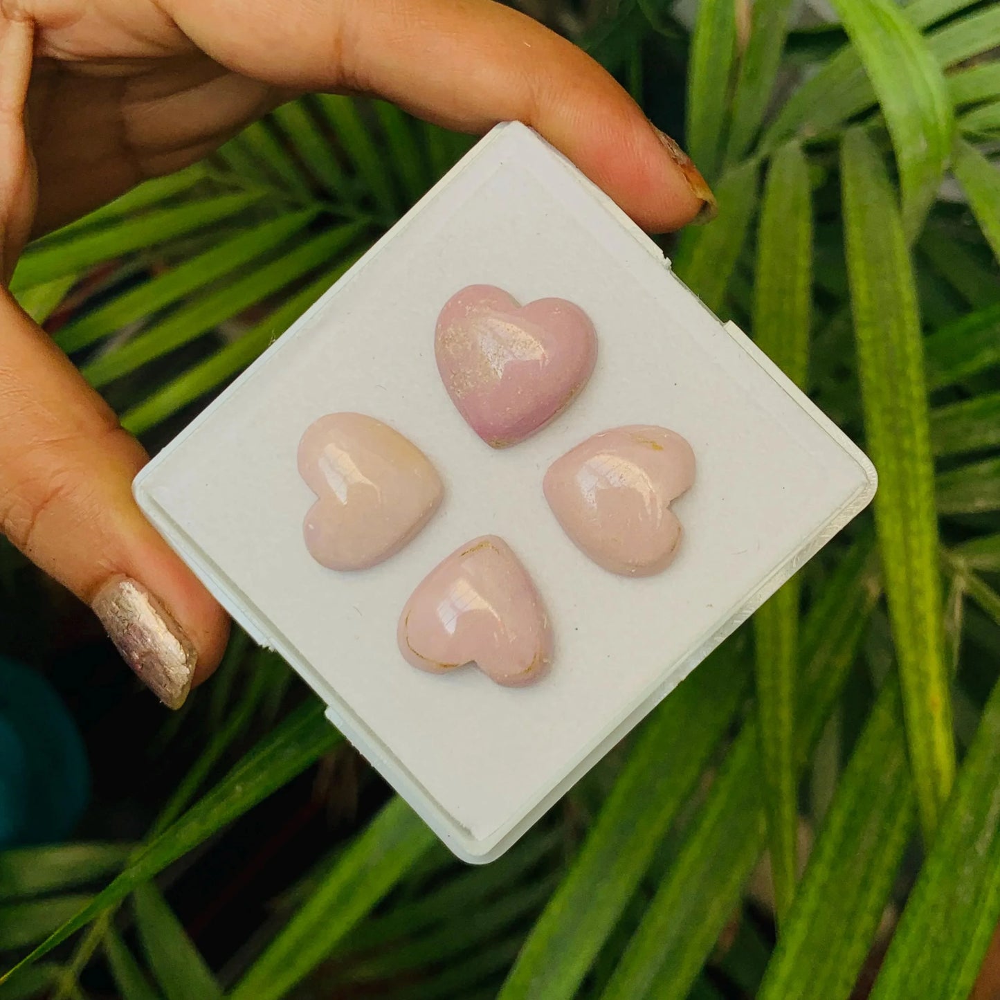 Hand holding four heart-shaped rose quartz cabochon gemstones on white display