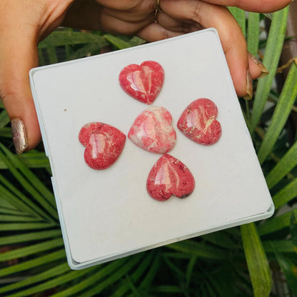 Hand holding tray with five pink heart-shaped natural gemstone cabochons outdoors