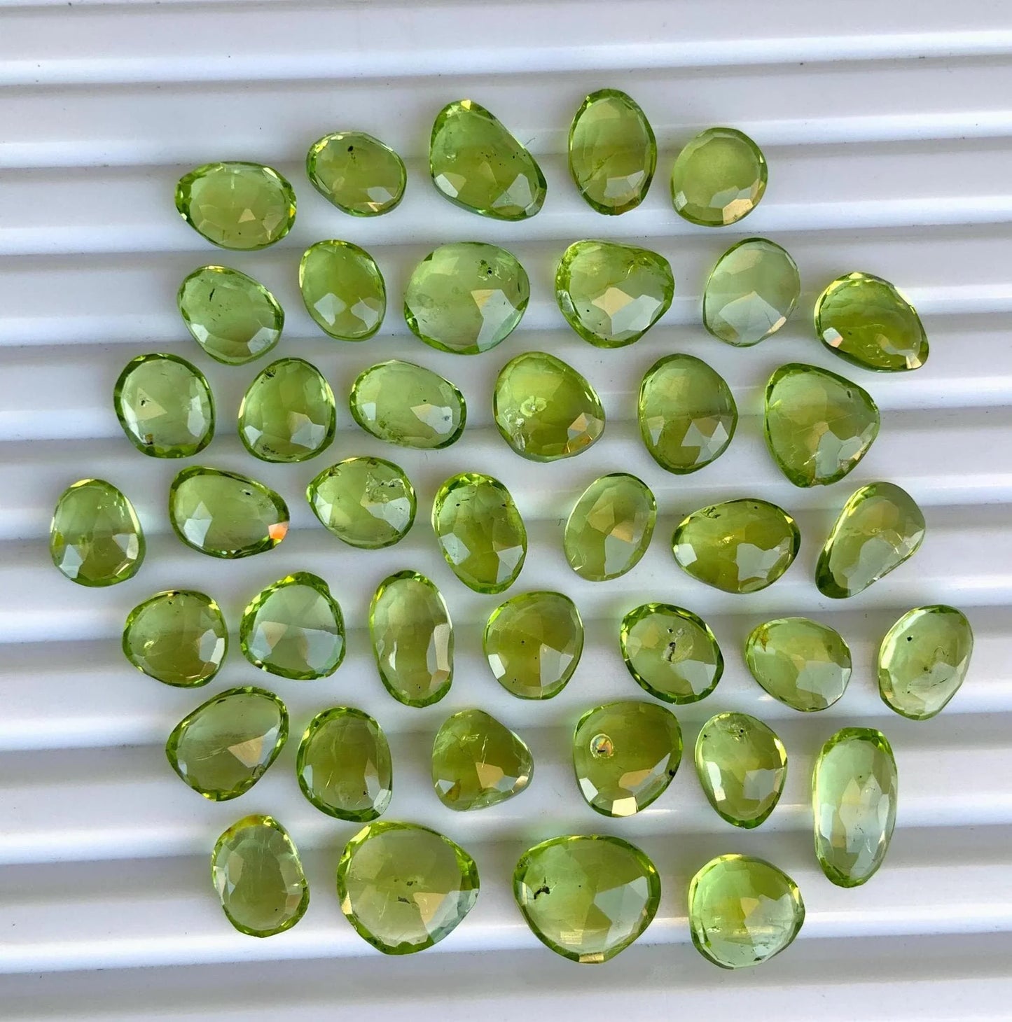 Faceted pear-shaped green peridot gemstone beads arranged on a white background