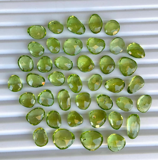 Faceted pear-shaped green peridot gemstone beads arranged on a white background