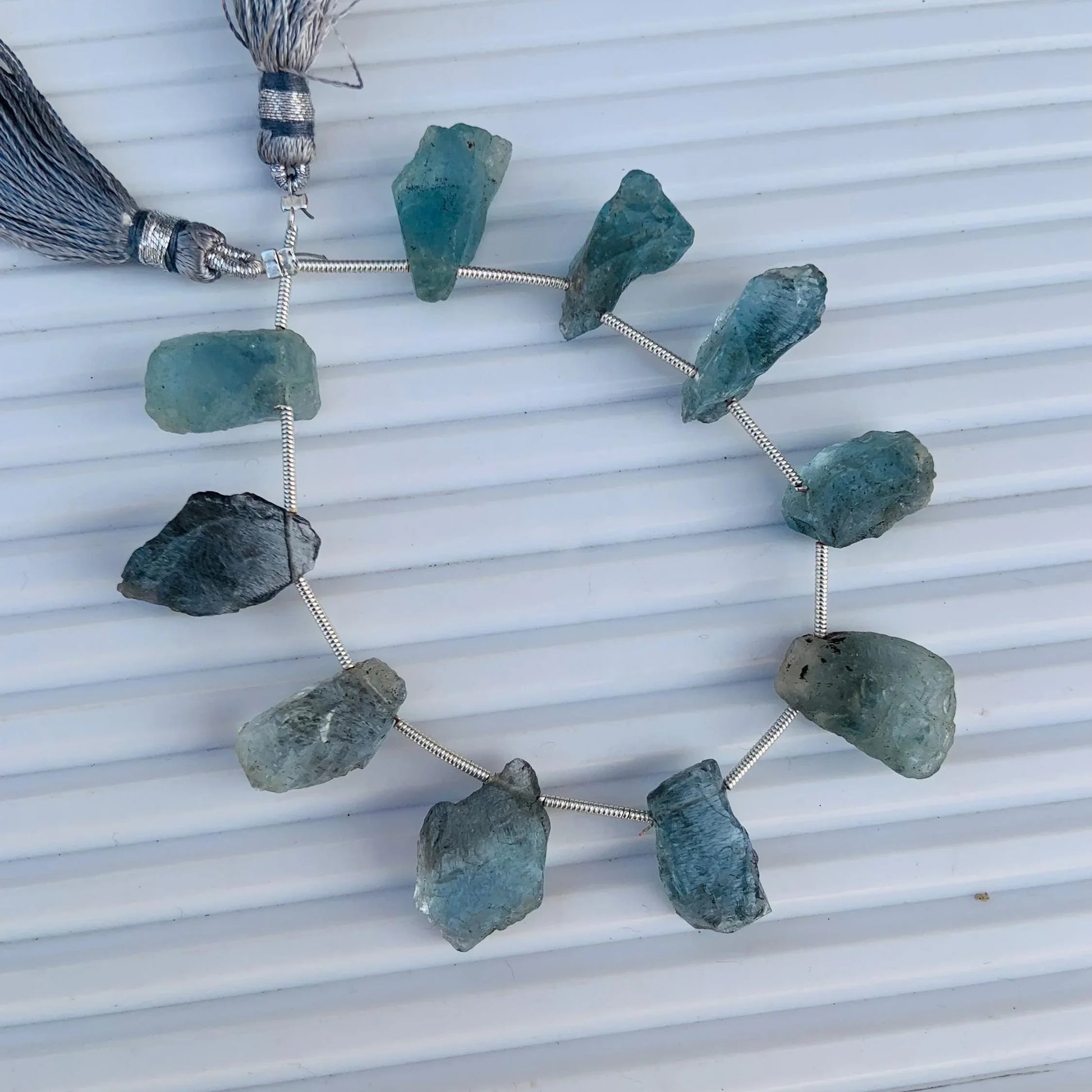 Strand of rough blue aquamarine gemstone beads with silver tassels on a white background