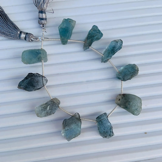 Strand of rough blue aquamarine gemstone beads with silver tassels on a white background