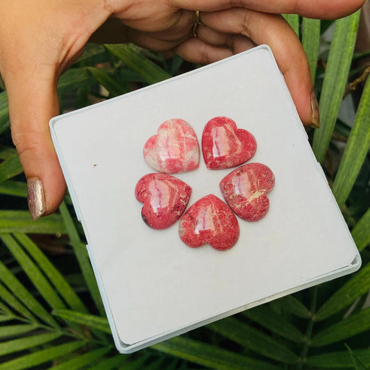 Hand holding box with five polished pink heart-shaped gemstone cabochons
