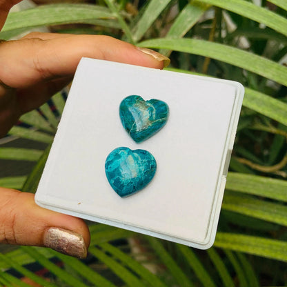 Pair of heart-shaped blue-green gemstone cabochons displayed on a white card outdoors