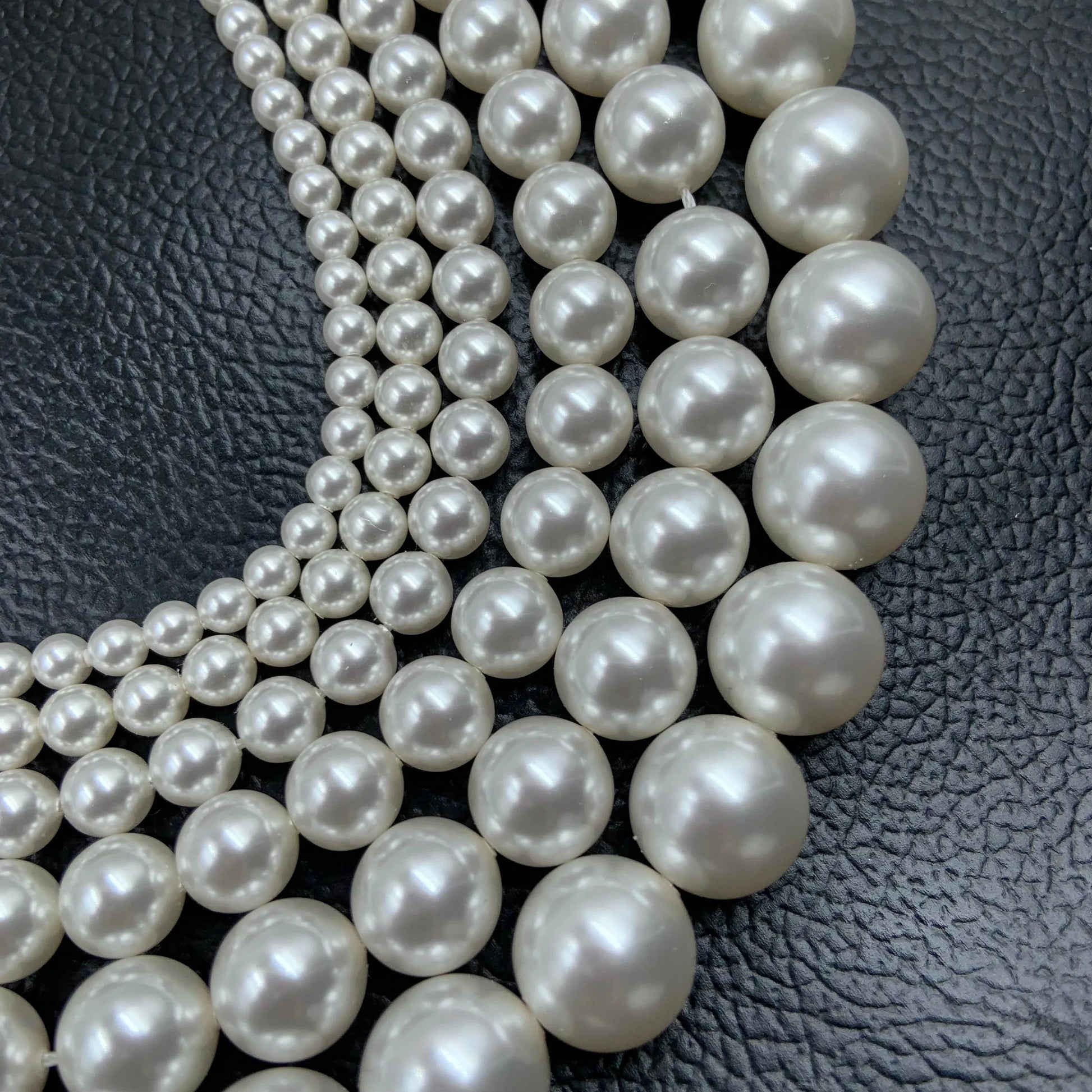 Strands of round white gemstone beads arranged on black textured leather