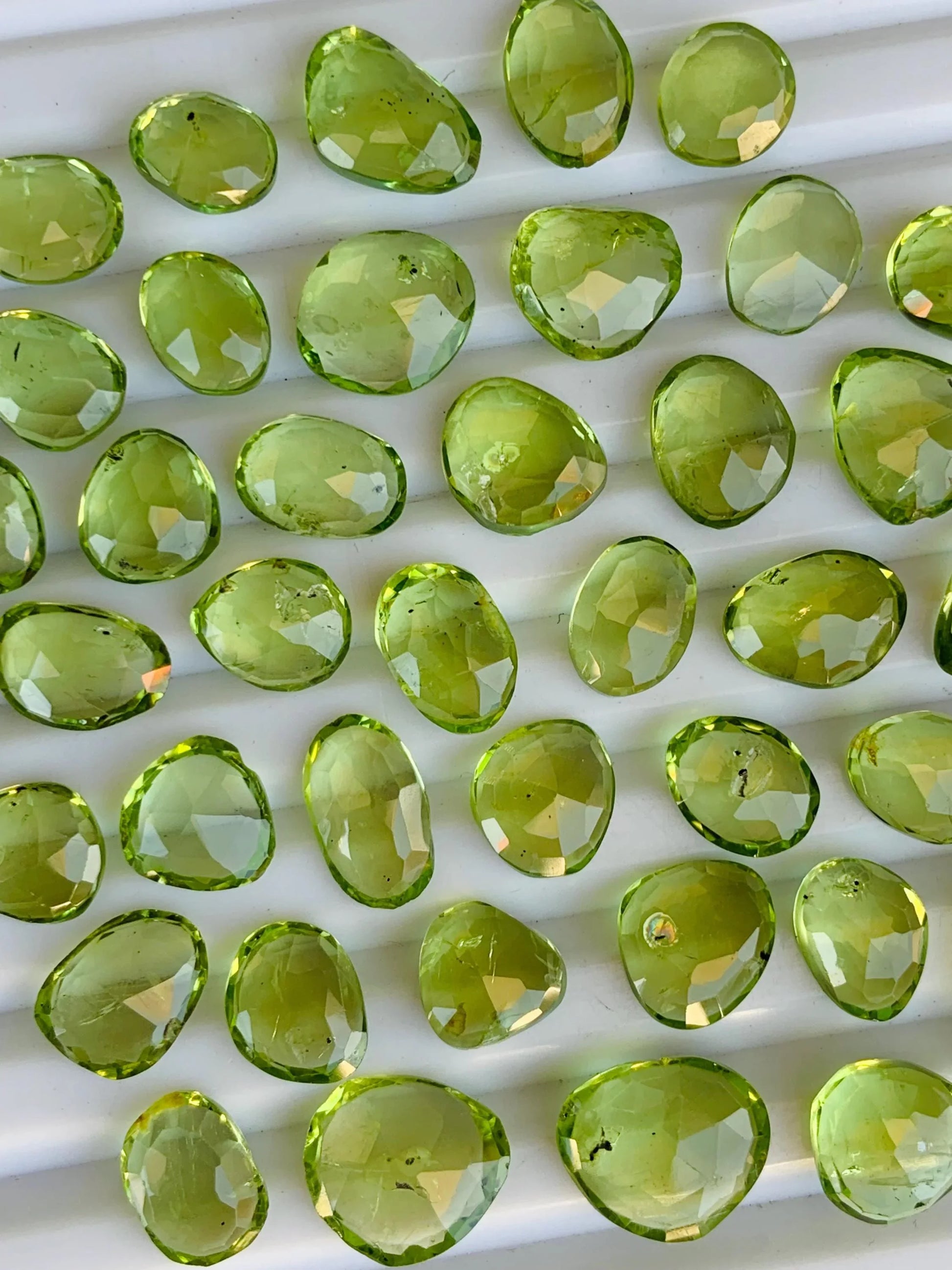 Faceted oval green peridot gemstone beads arranged on a white ridged tray
