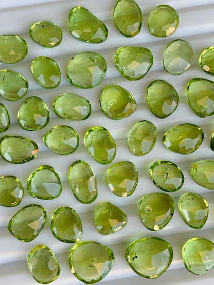 Faceted oval green peridot gemstone beads arranged on a white ridged tray