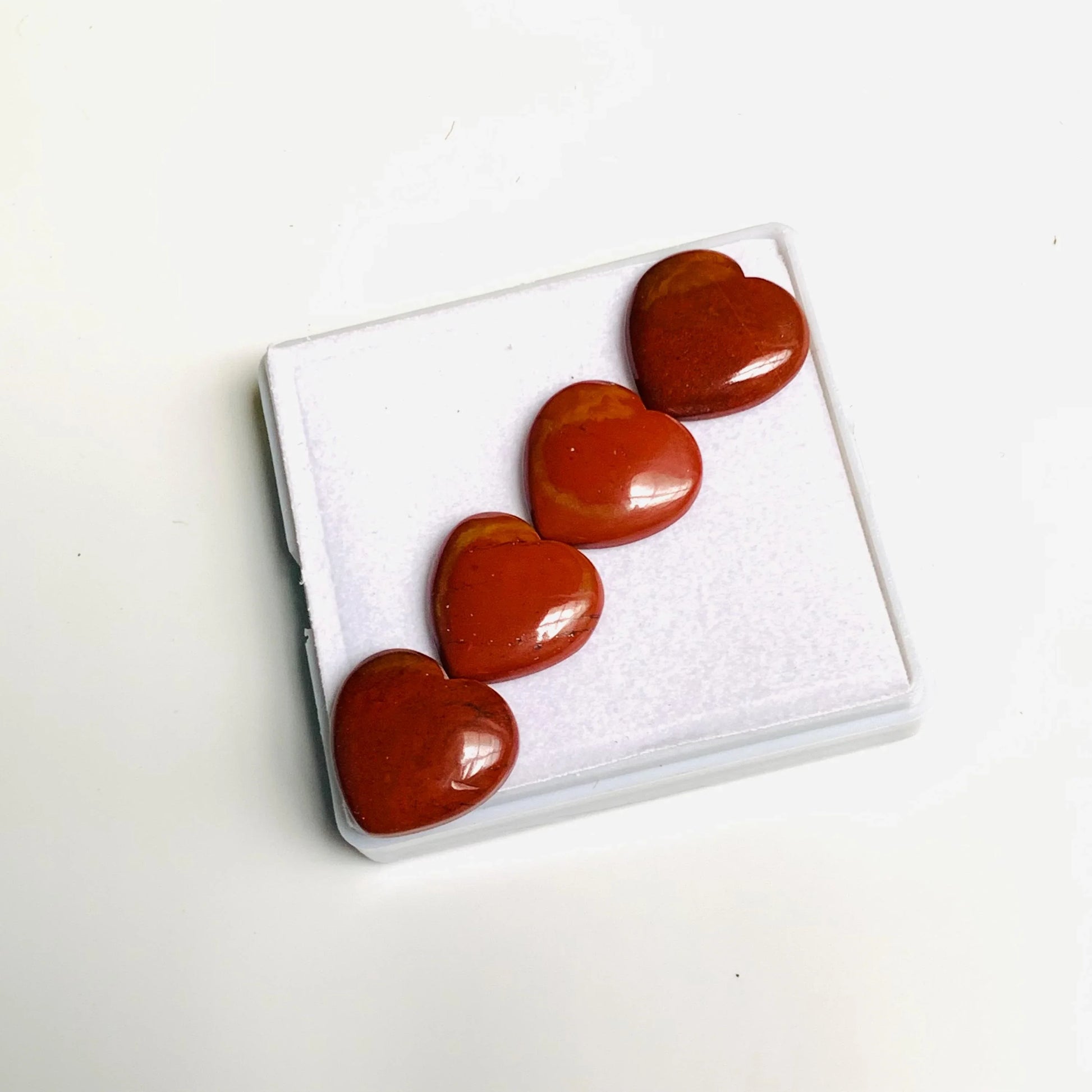 Four red jasper heart-shaped gemstone cabochons on a white display box