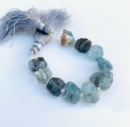 Strand of rough aquamarine gemstone beads with light blue tassels on white background